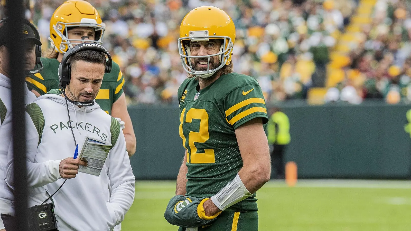 Matt LaFleur in a headset reading a play sheet beside Aaron Rodgers on the Lambeau Field sideline