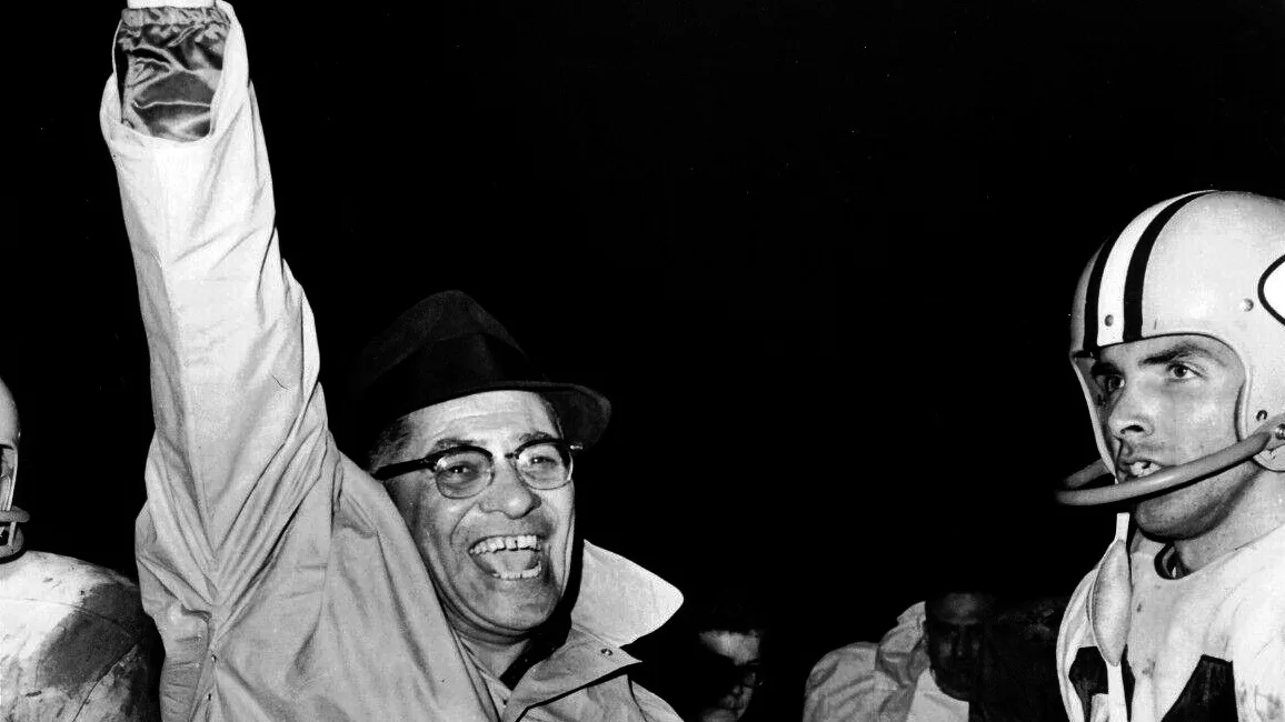 Vince Lombardi raising his fist and smiling beside his players